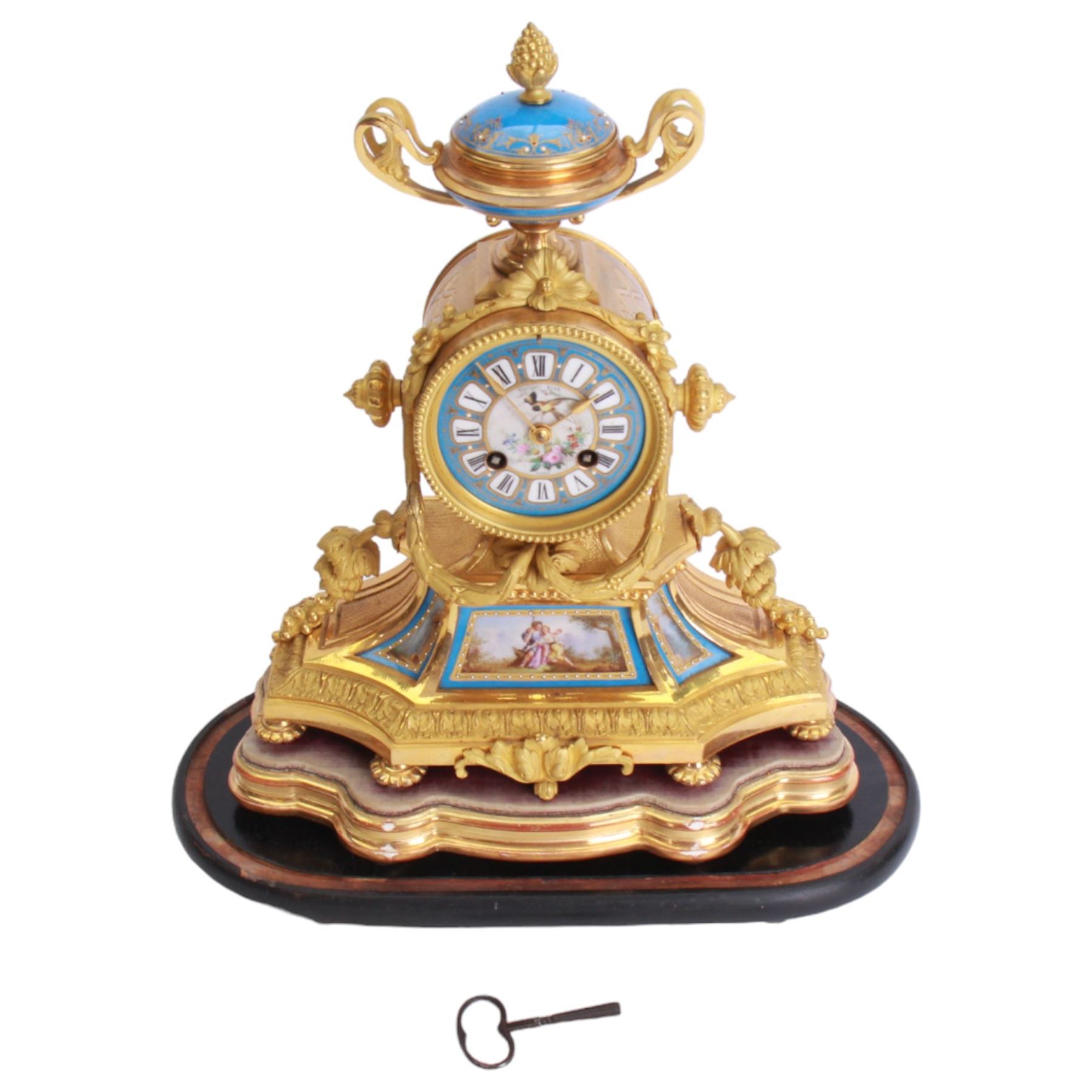 French - 19th century Sevres style porcelain inset 8-day mantle clock with an over out swept base and foliate scrolls,  porcelain panels painted with romantic scenes within gilt highlighted blue borders, dial surmounted by a conforming oval porcelain urn with side handles, blue porcelain dial with a painted centre and contrasting white cartouche Roman numerals and gilt spade hands, dial inscribed Thomas Kirk, Paris, with a rack striking twin train movement, striking the hours and half hours on a bell, mounted on a gesso padded base and ebonised plinth. With key and pendulum.