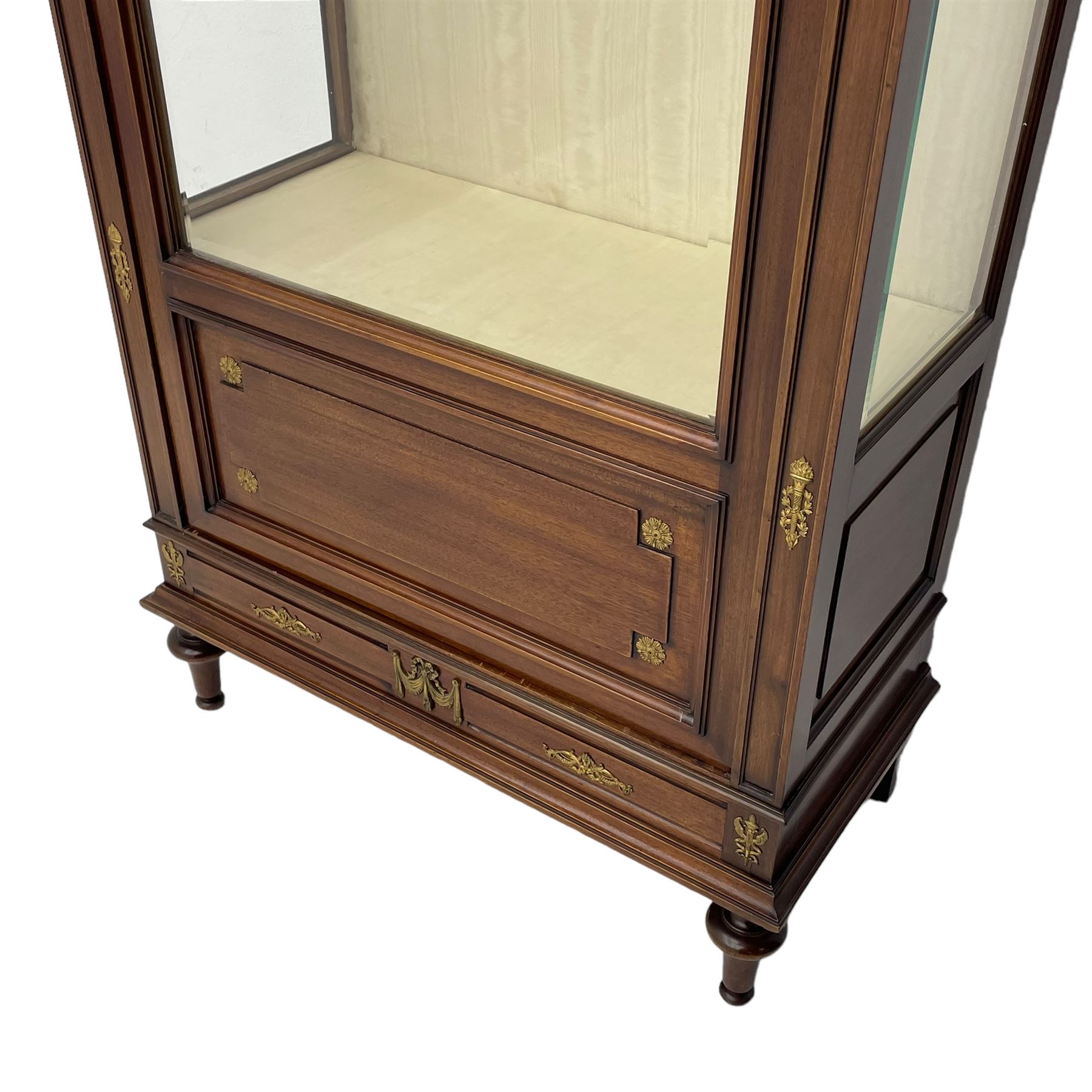 Early 20th century Louis XVI design mahogany vitrine display cabinet, projecting stepped cornice over recessed frieze decorated with gilt metal mounts of festoons and a bellflower wreath, fabric lined interior with two glass shelves, enclosed by bevel glazed door with lower panel, on two turned front feet 