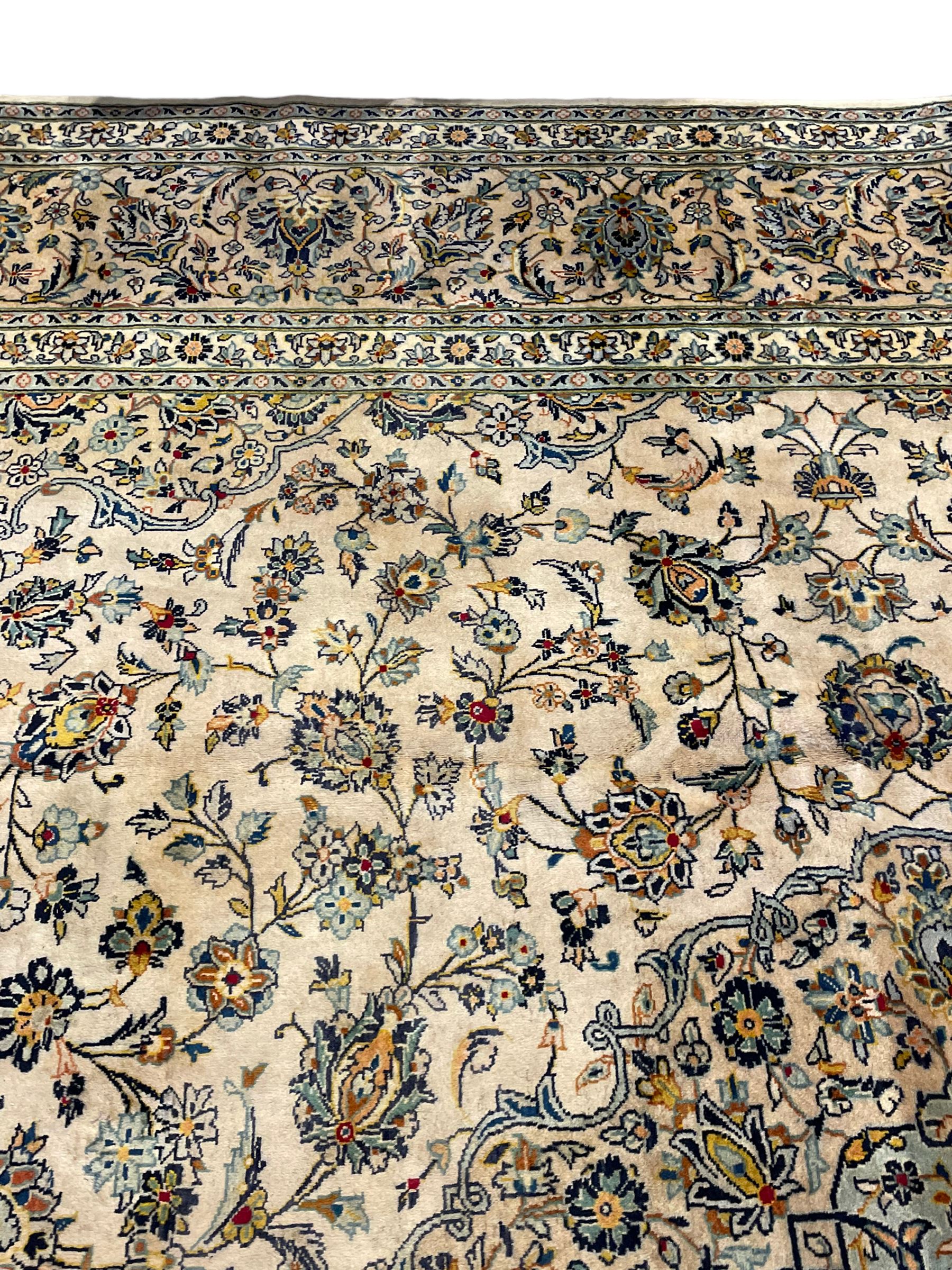 Central Persian Kashan pale khaki ground carpet, shaped central medallion enclosing small stylised motifs, the field decorated profusely with trailing foliate branches and plant motifs, guarded border with repeating floral design 