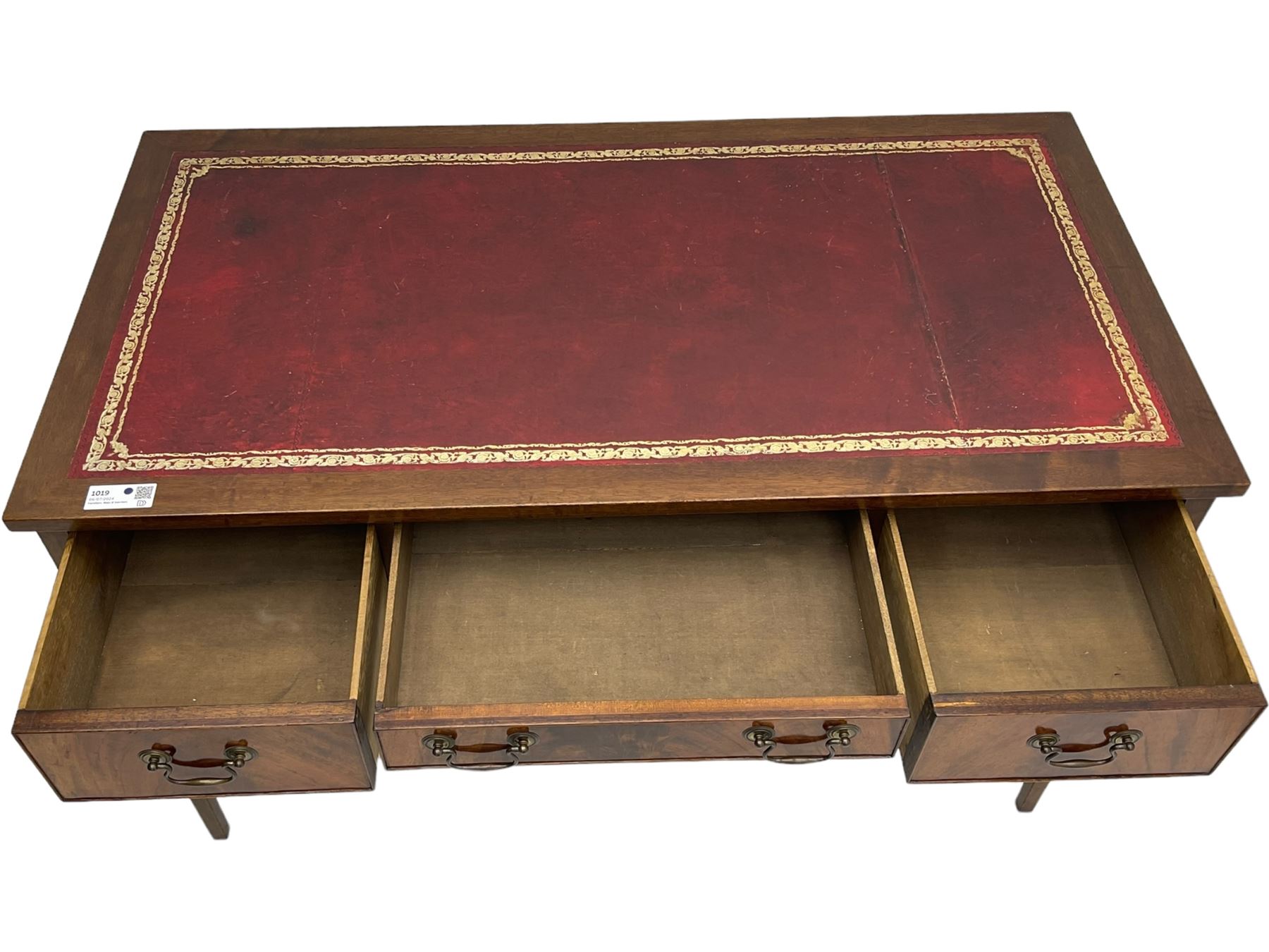 Mid-to-late 20th century mahogany writing desk, the rectangular top with a tooled red leather insert bordered with gilt detailing, three cock-beaded drawers with brass handles, the narrow central drawer flanked by two wider drawers, standing on square tapered legs