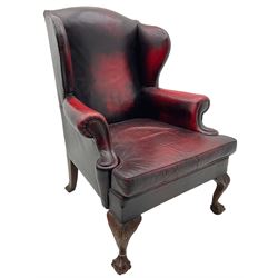 Georgian design hardwood-framed wingback armchair, upholstered in red leather, loose seat cushion and rolled arms, on acanthus carved ball and claw front feet 