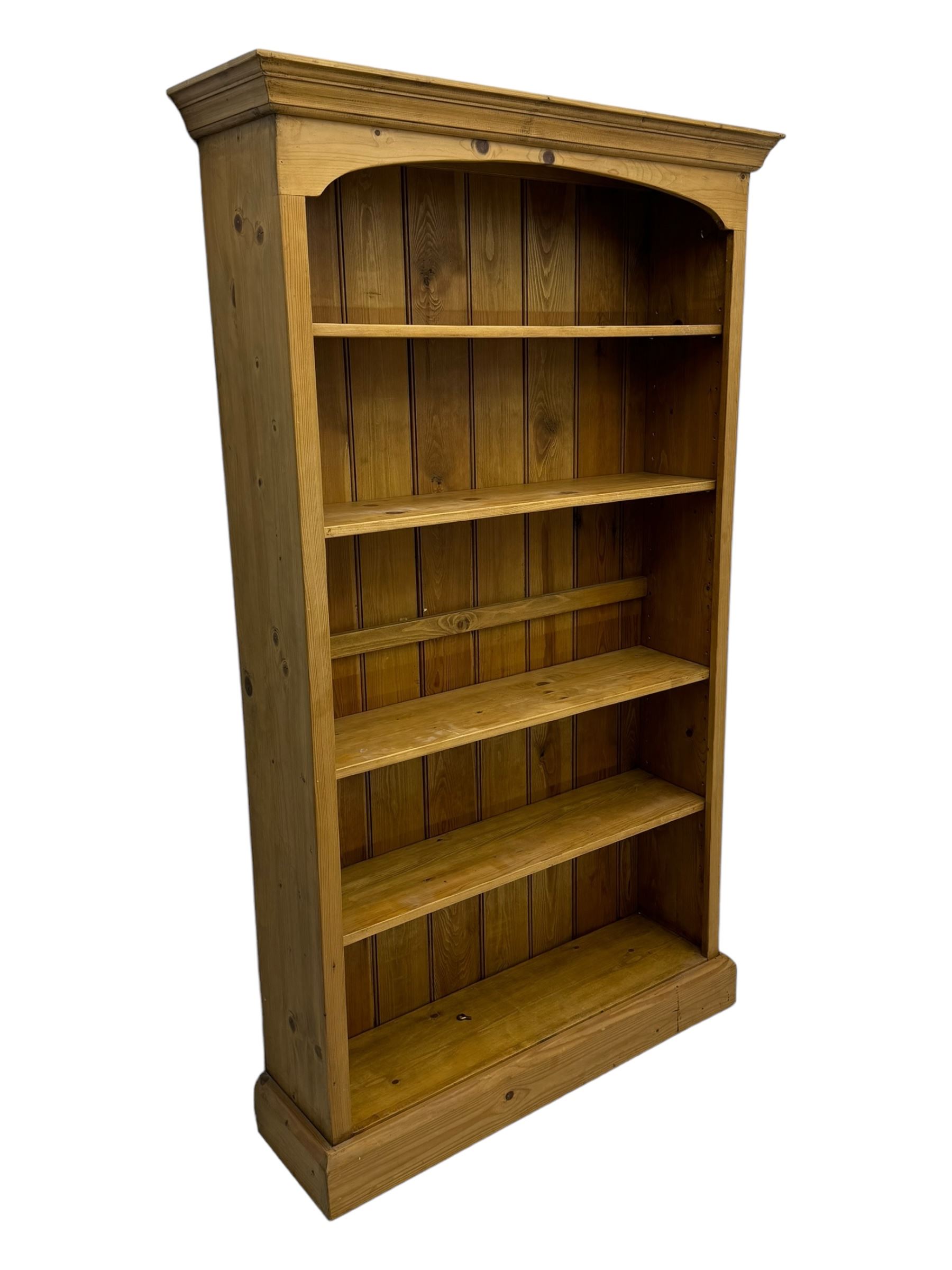 Pine open bookcase, projecting moulded cornice over arched frieze, fitted with four adjustable shelves, on plinth base