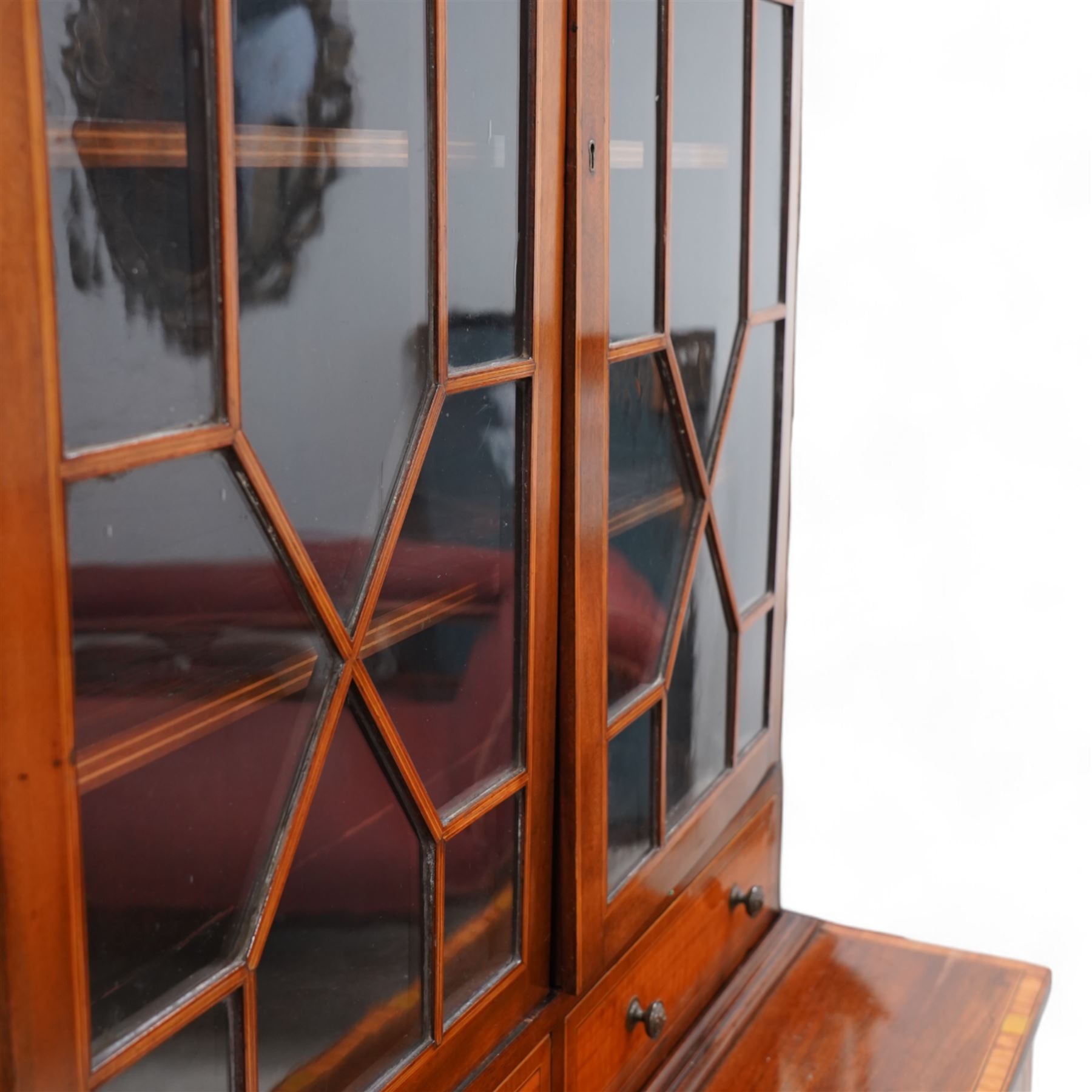 Early 19th century mahogany and satinwood bookcase on stand, scrolled swan neck pediment with pierced panels, satinwood frieze over two astragal glazed doors enclosing adjustable shelves, fitted with two drawers, the stand with rectangular satinwood banded top over frieze inlaid with central shell panel and extending bell flower festoons, on square tapering supports united by undertier with raised gallery 