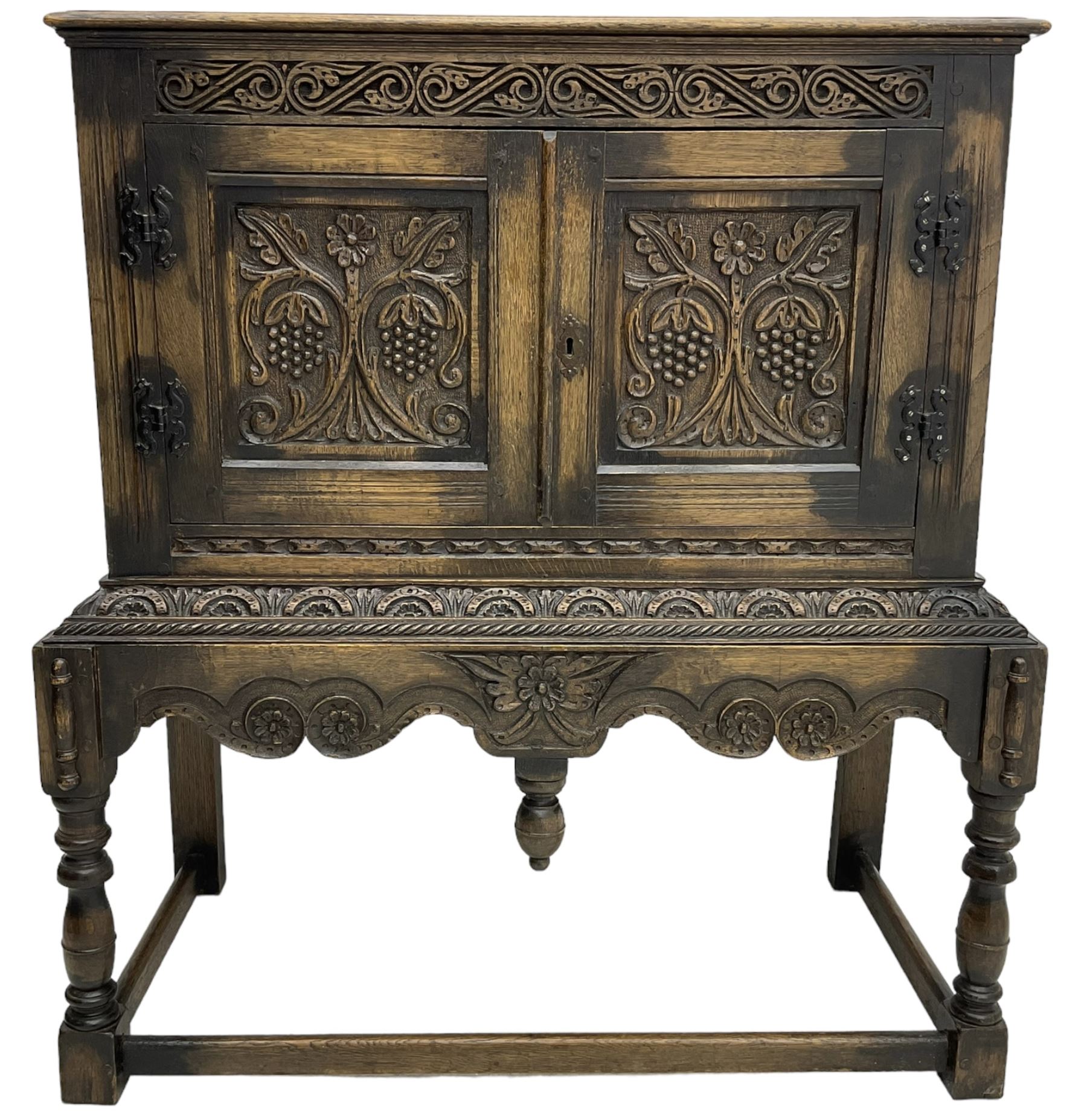 Jacobean Revival carved oak cupboard, moulded rectangular top over S-scroll carved frieze and two doors, the panelled doors carved with stylised plant motifs, on stand decorated with lunettes and shaped apron with hanging turned pendant, on turned supports united by stretchers 