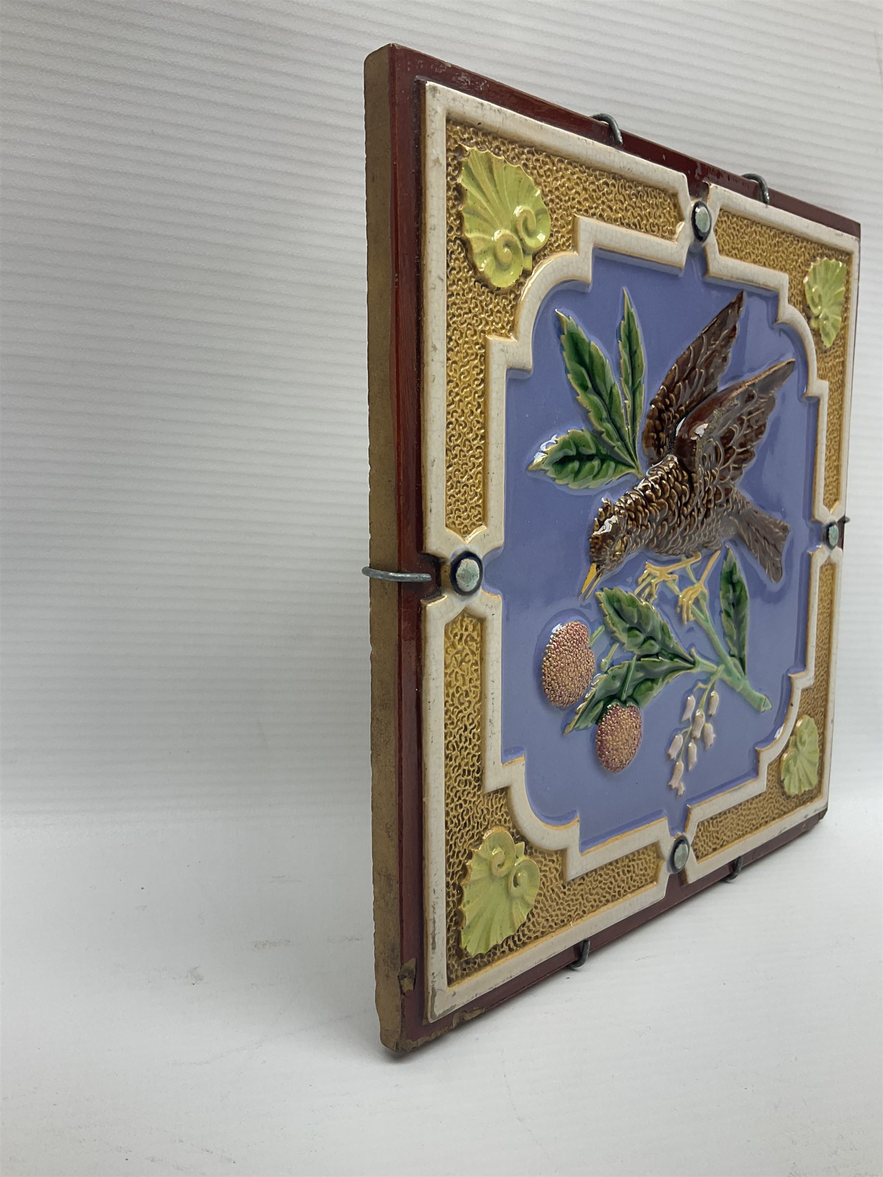 19th century Minton & Co majolica tile, decorated in relief with a bird upon a fruiting branch against a blue ground, with textured ochre border and anthemion to each corner, impressed mark verso, H19.7cm