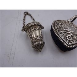 Edwardian silver pin cushion, in the form of a heart, with embossed floral decoration, with blue pin cushion between two heart shaped silver covers, with chatelain hook, hallmarked Henry Matthews, Birmingham 1902, together with a late Victorian silver thimble holder, embossed with scrolling decoration and with velvet interior, with chatelain chain, hallmarked Levi & Salaman, Birmingham 1899, pin cushion H4.5cm