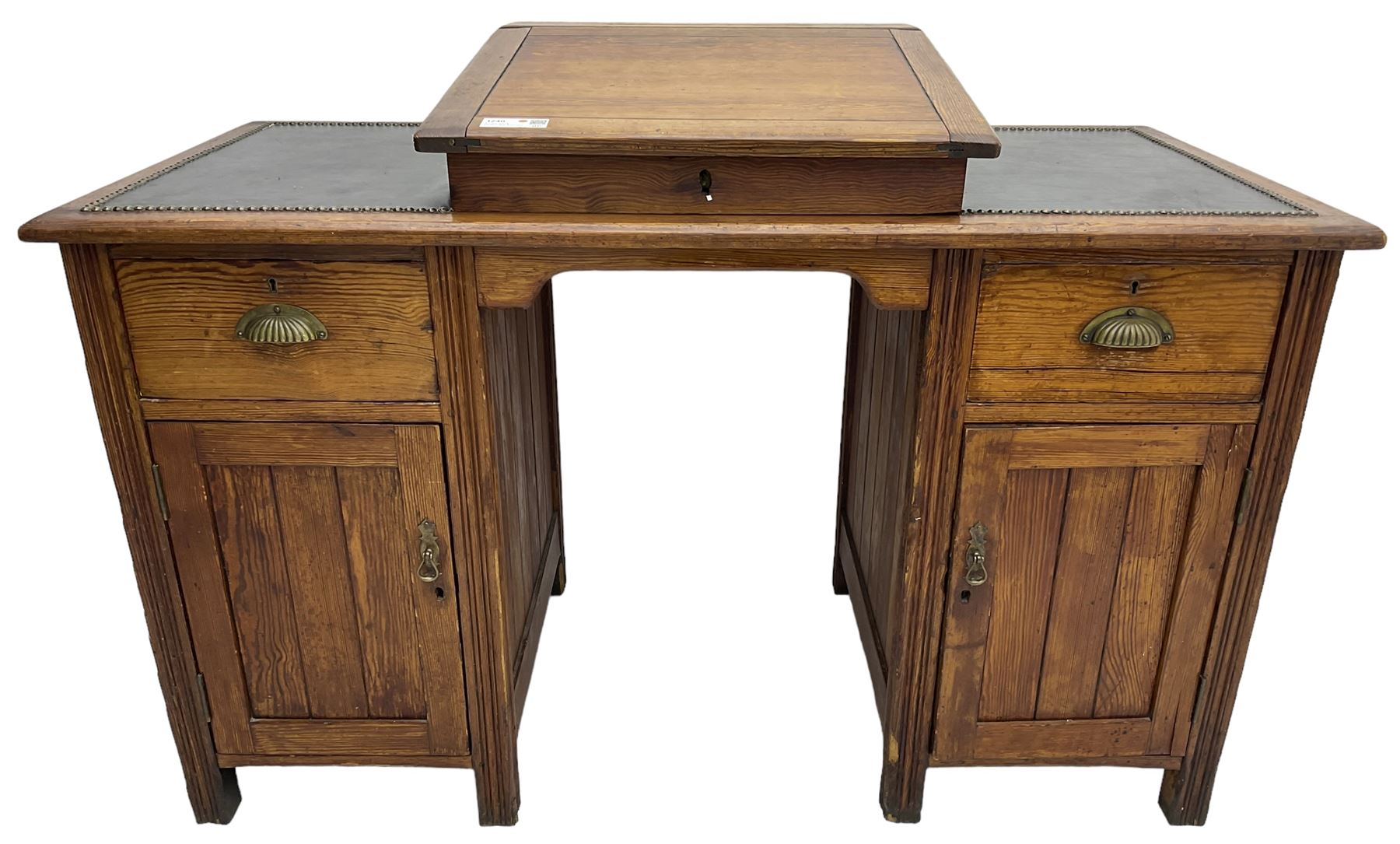 Edwardian pitch pine desk, rectangular top with writing slope flanked by inset leather writing surfaces, over twin pedestals each with shell cup handled drawer over cupboard, the left enclosing two shelves, the right enclosing sliding trays, on fluted straight supports